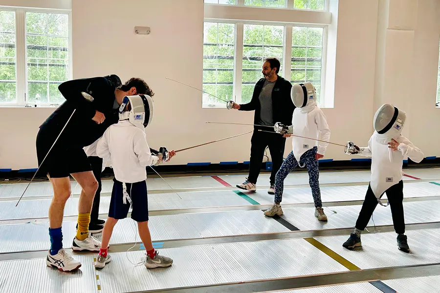Fencing coaches guide young épée students during a kids’ class at Allez Fencing Club in Watertown, MA, focusing on technique, positioning, and confidence building.
