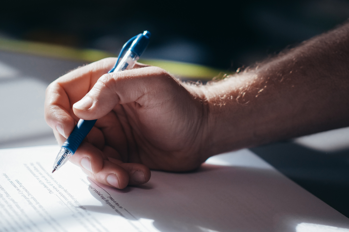 En hand håller en blå penna och skriver på ett pappersdokument.