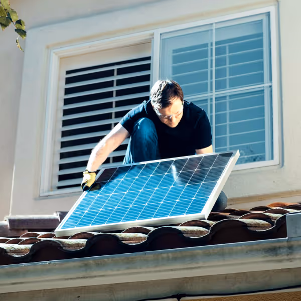 Un homme installe un panneau solaire sur le toit d'une maison ensoleillée.