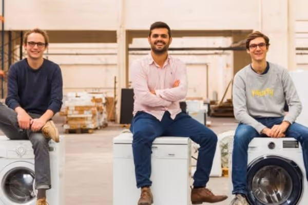 Trois membres de l’équipe Murfy assis sur des machines à laver dans un entrepôt, souriants et détendus.