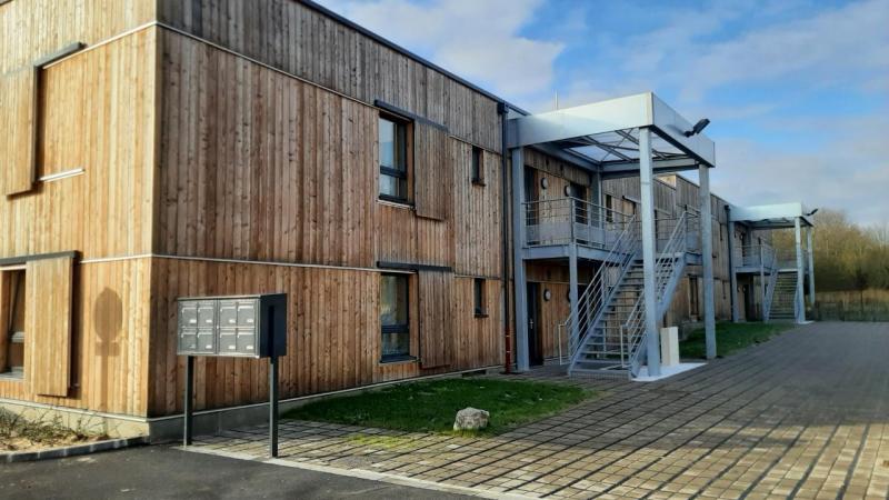 Résidence à façade bois avec escalier métallique extérieur, sous un ciel légèrement nuageux.