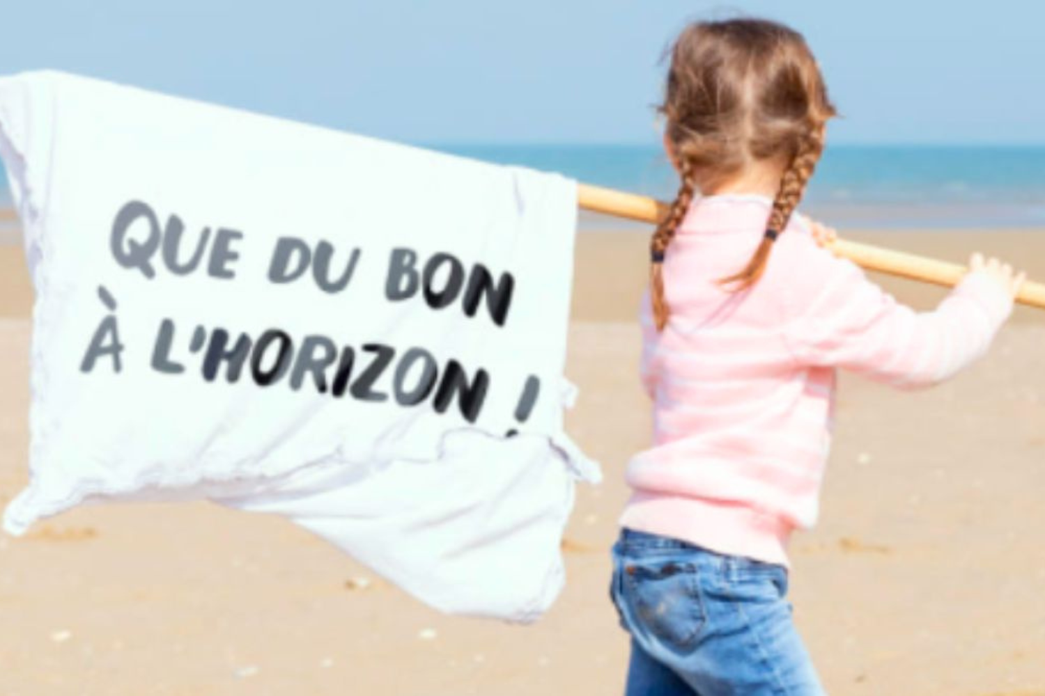 Petite fille de dos sur une plage, tenant un grand drapeau blanc fixé à un bâton. Le drapeau porte l’inscription en lettres noires : « QUE DU BON À L’HORIZON ! ». L’enfant porte un pull rose clair et un jean, ses cheveux sont attachés en deux tresses. En arrière-plan, sable et mer sous un ciel dégagé.