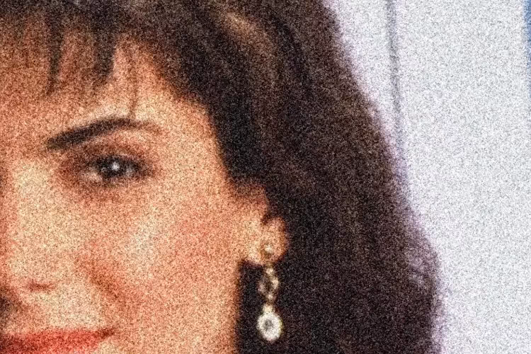 Portrait d'une femme brune au style rétro, vu partiellement (gauche du visage uniquement visible), avec des cheveux volumineux, une frange, un rouge à lèvres vif et une paire de boucles d’oreilles pendantes dorées avec pierres blanches. L’image est très granuleuse, avec un effet de bruit ou de flou qui lui donne un aspect vintage ou délibérément vieilli.