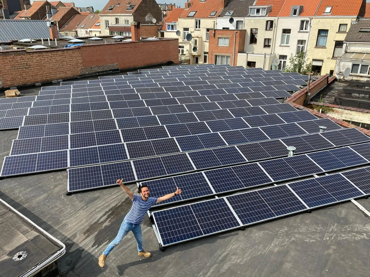 Homme souriant devant une grande installation de panneaux solaires en toiture.