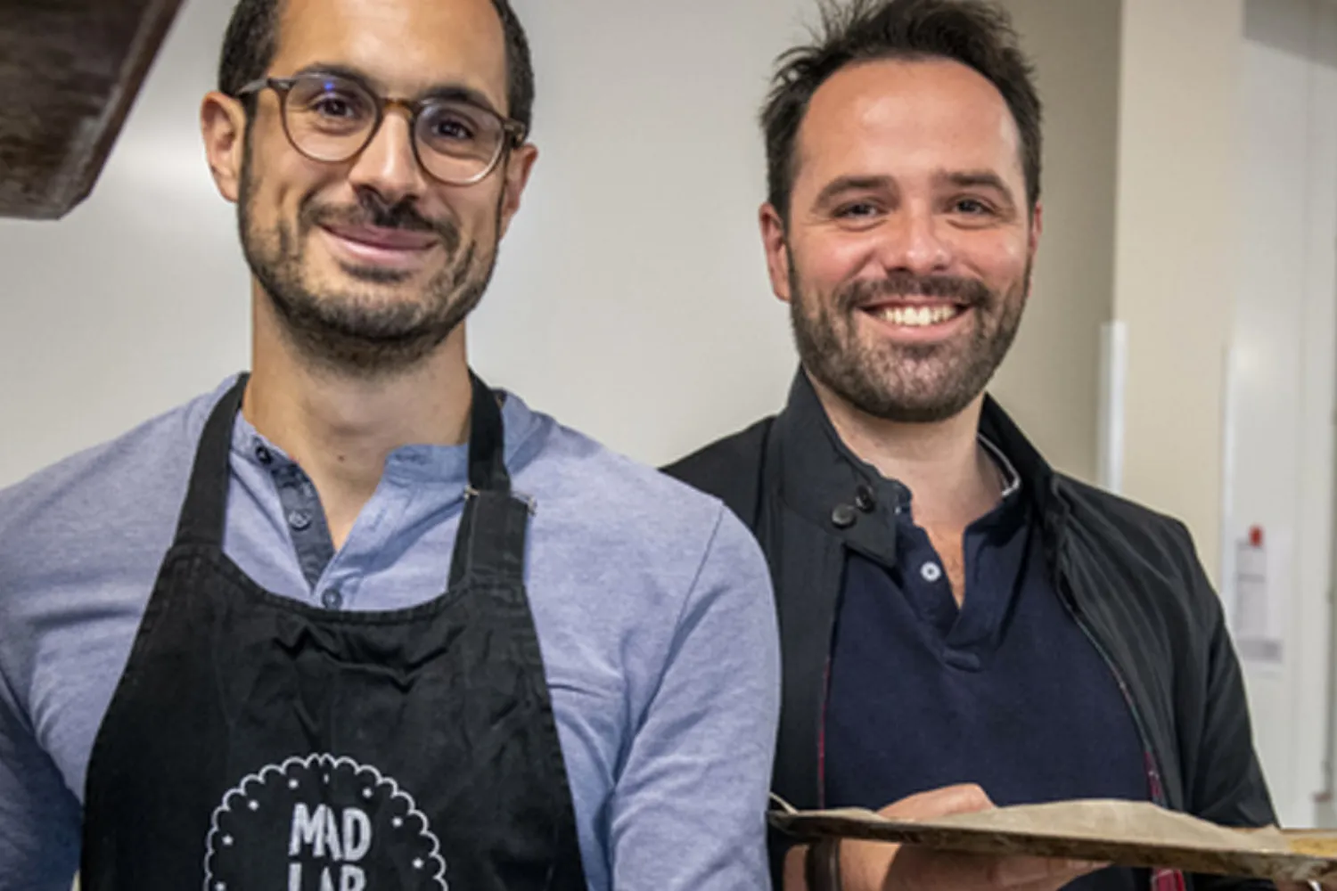 Deux hommes souriants, dont un porte un tablier Madlab.