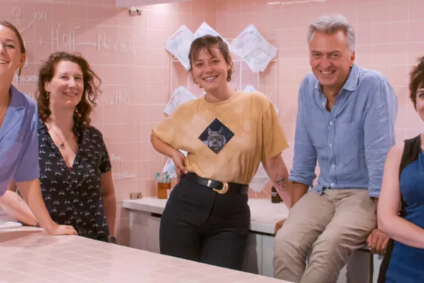 Membres de l’équipe de La Ressource souriant autour d’un comptoir, devant un mur carrelé rose.