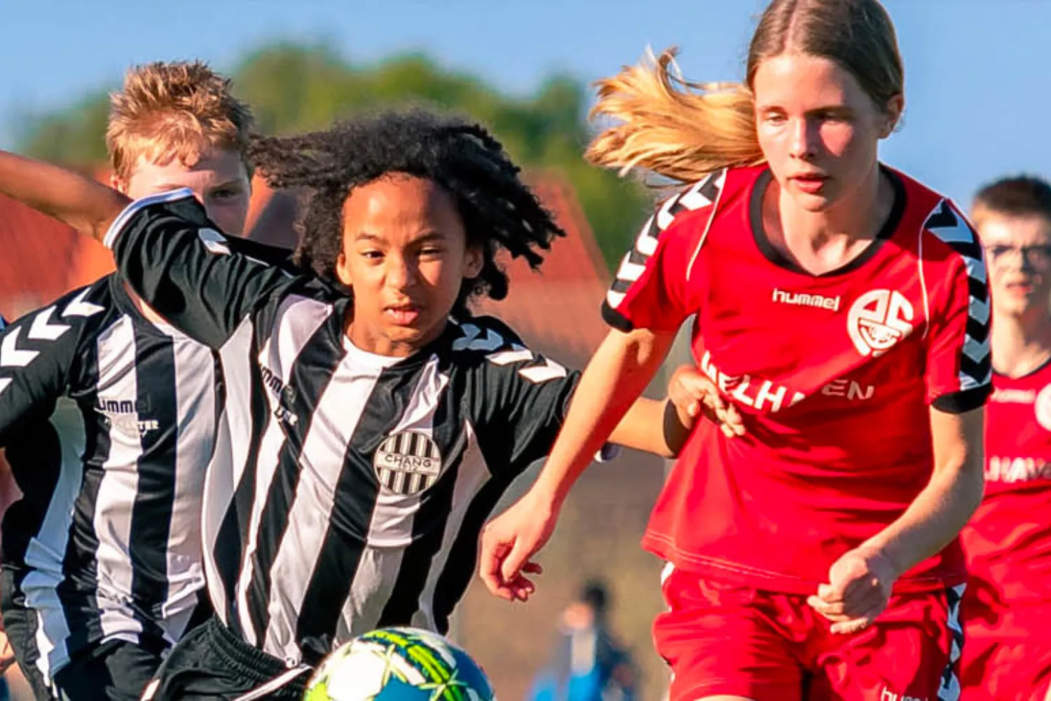 Jeunes footballeurs en plein match, un joueur en noir et blanc disputant le ballon face à une joueuse en rouge