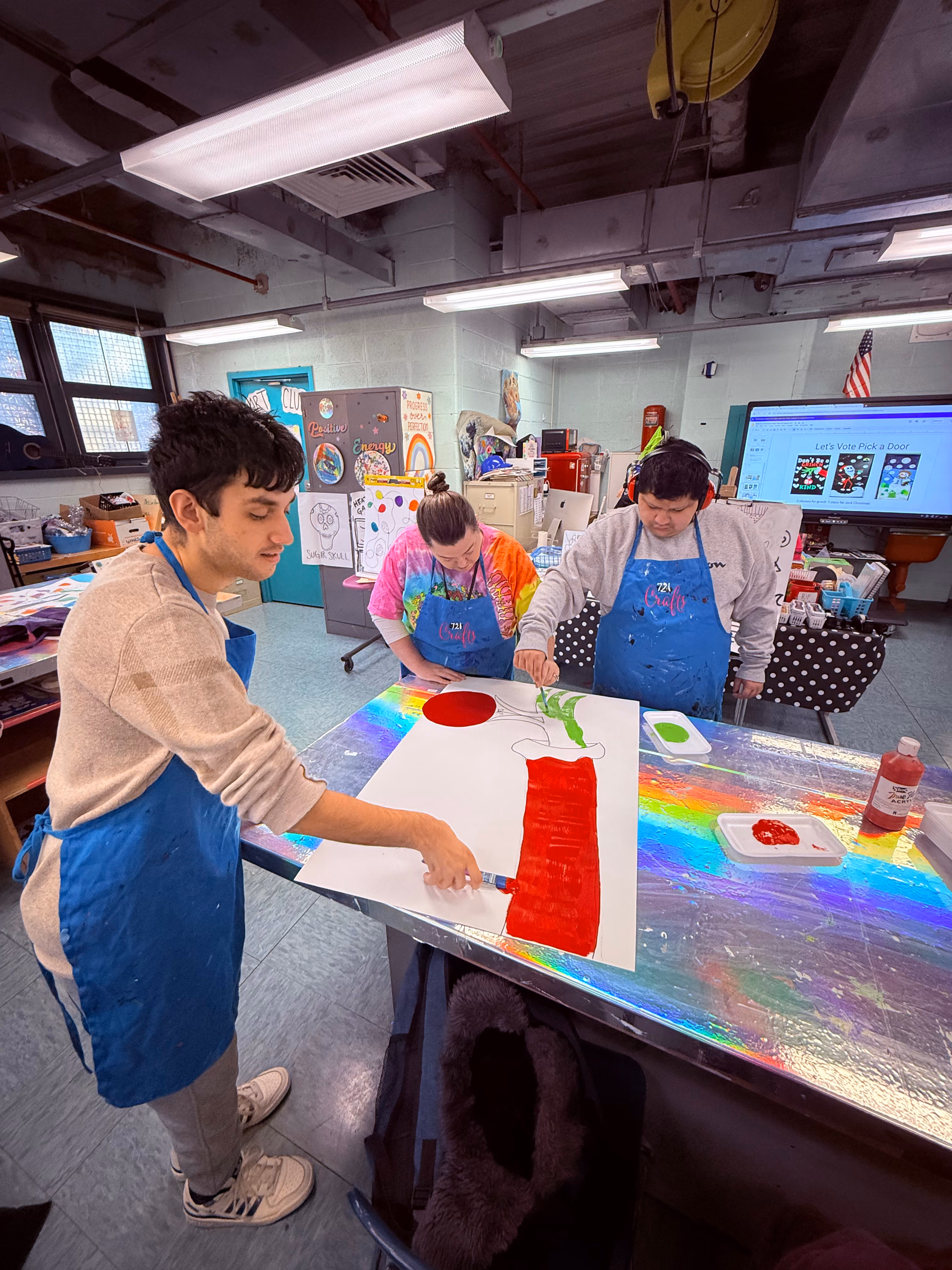 Three students in aprons painting a large canvas in art class