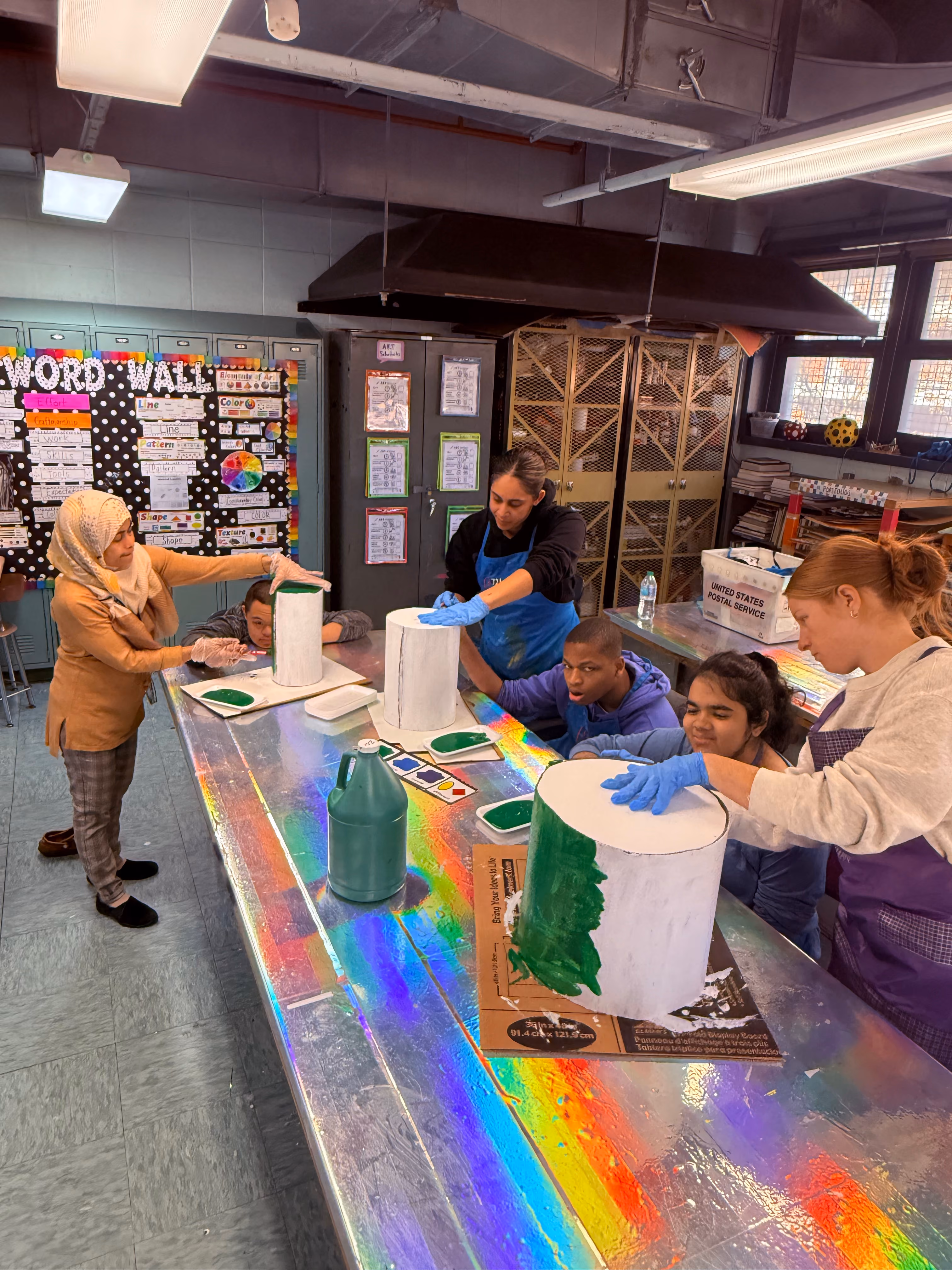Students and teachers painting cylindrical sculptures in art class