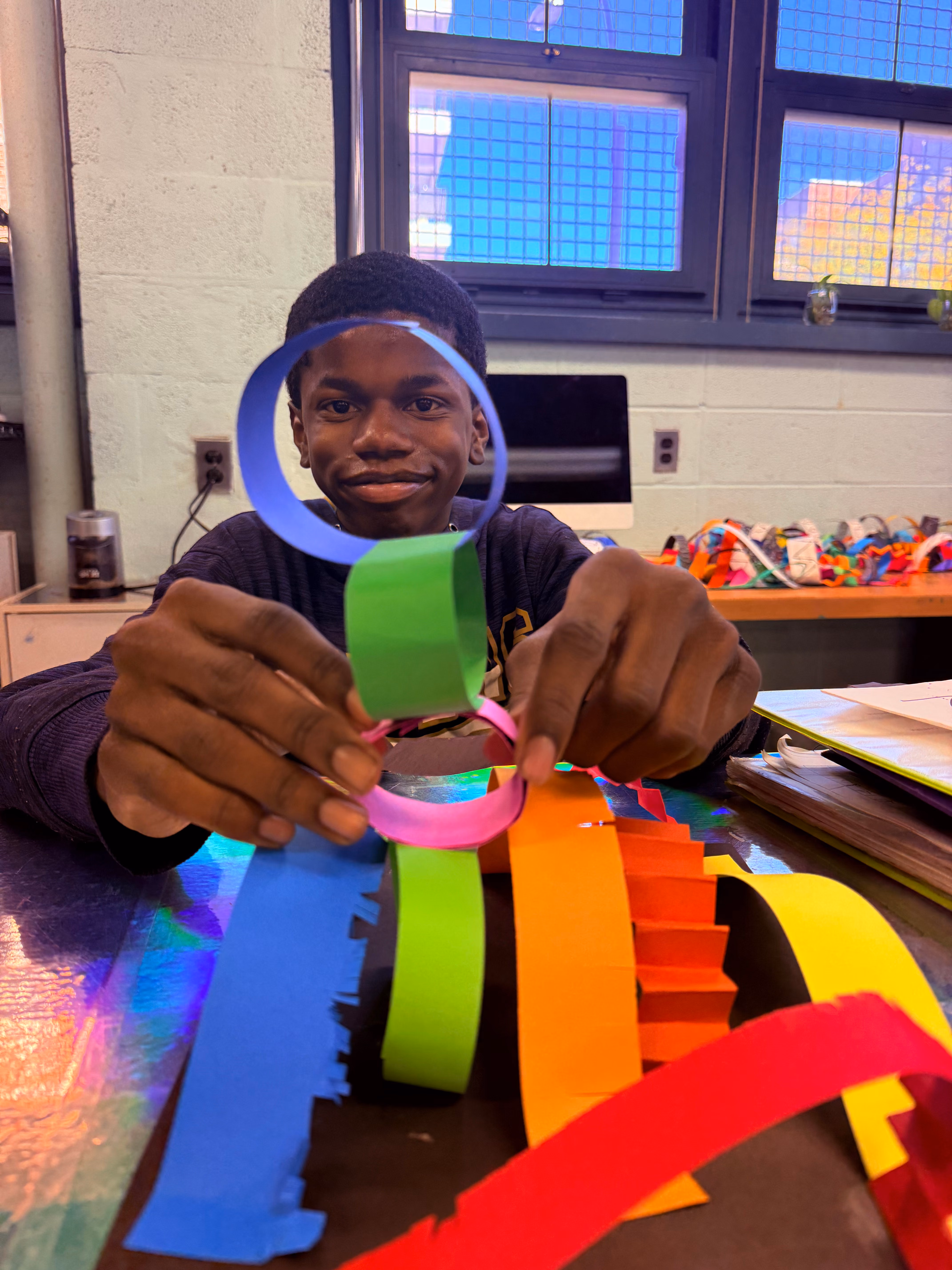 Student smiling while building a colorful paper chain link sculpture