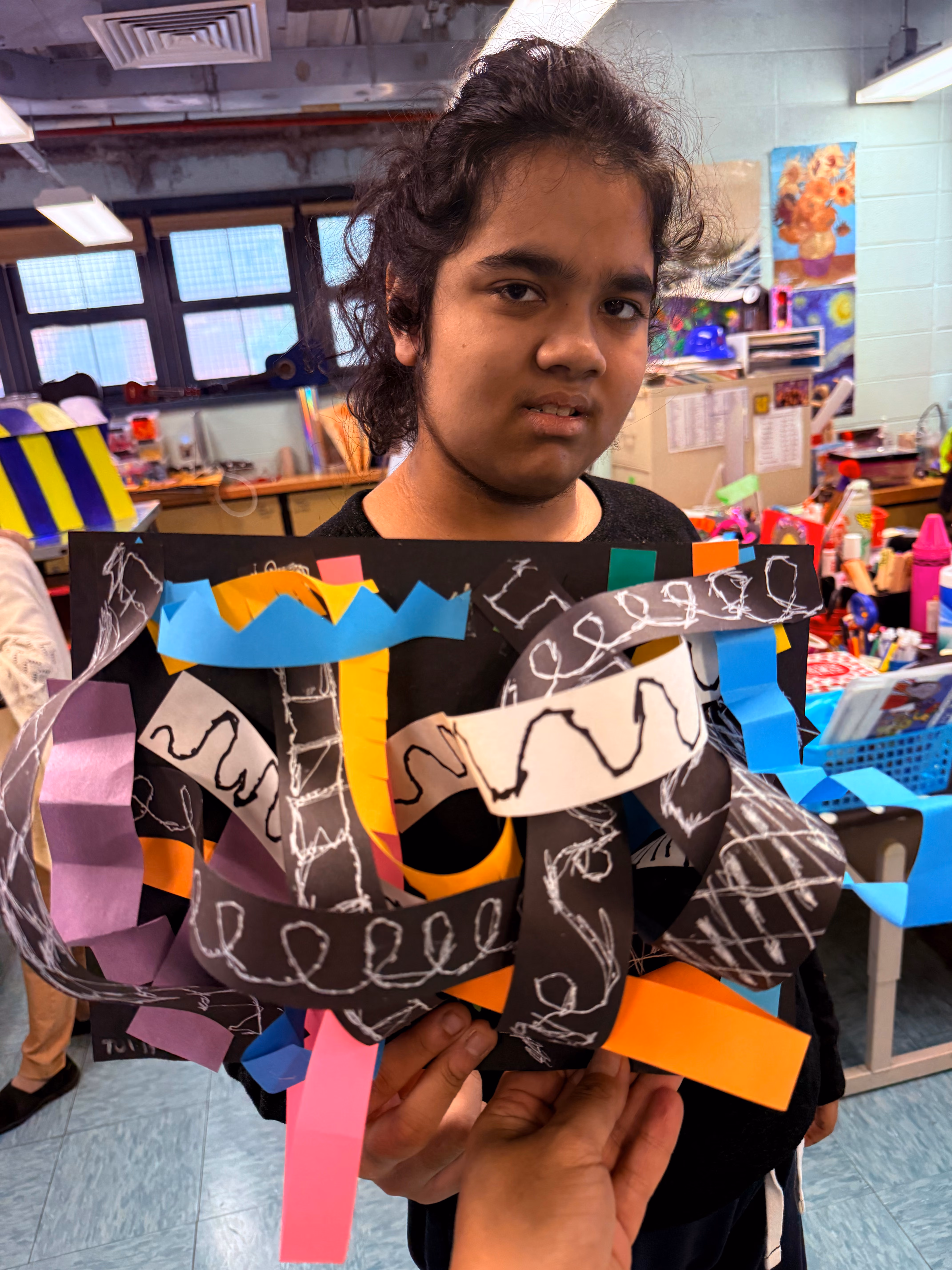 Student displaying colorful paper sculpture artwork in art classroom