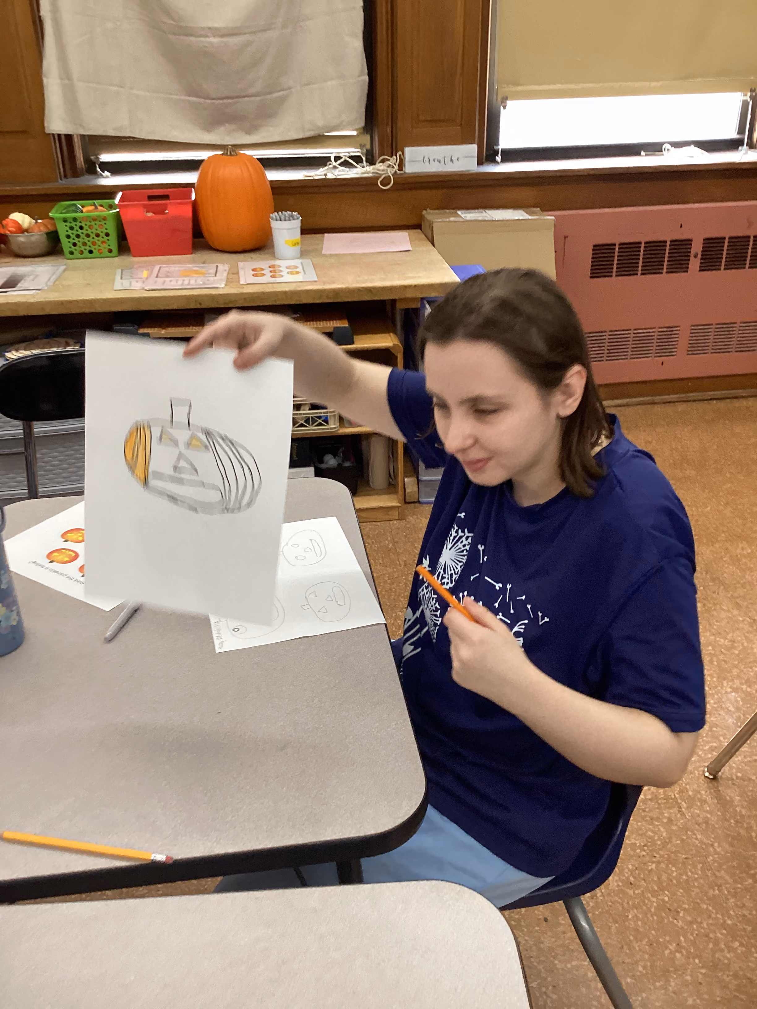 Student holds up pencil drawing of a pumpkin in art class