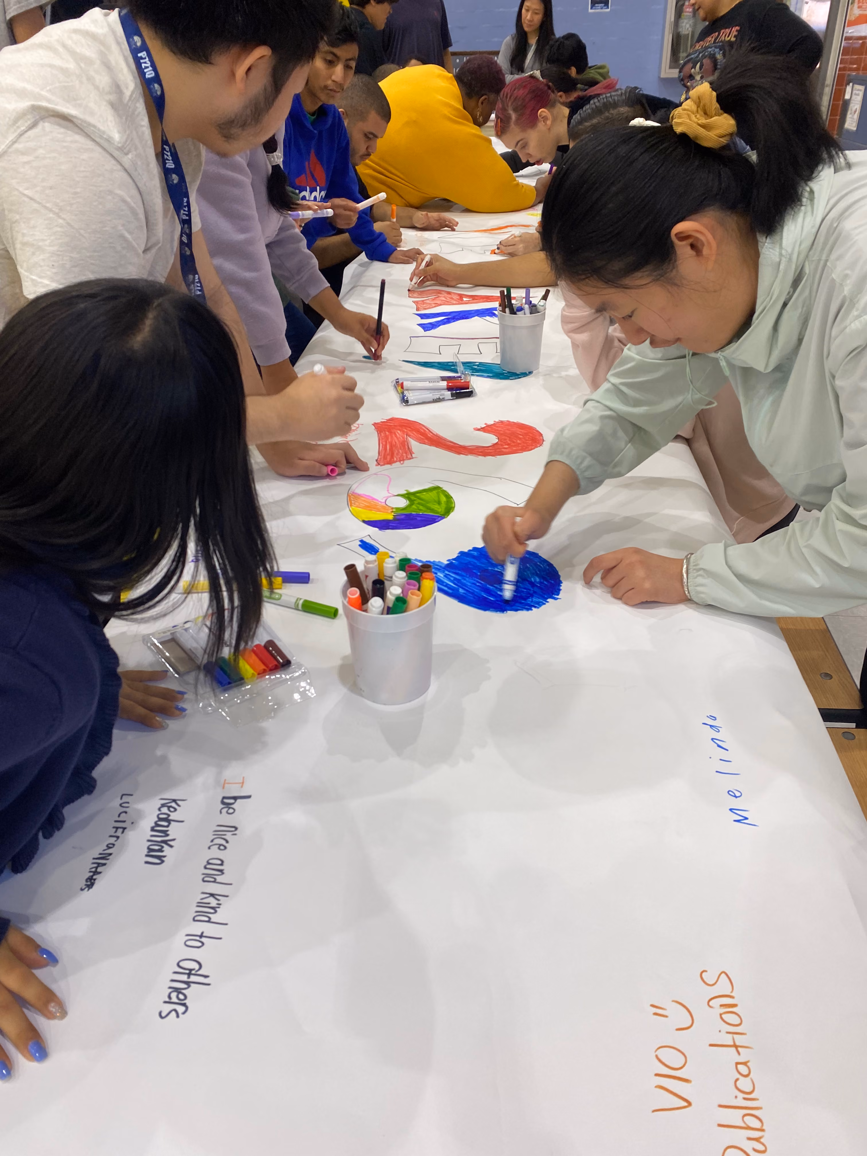 Students drawing and writing on a large collaborative mural with markers