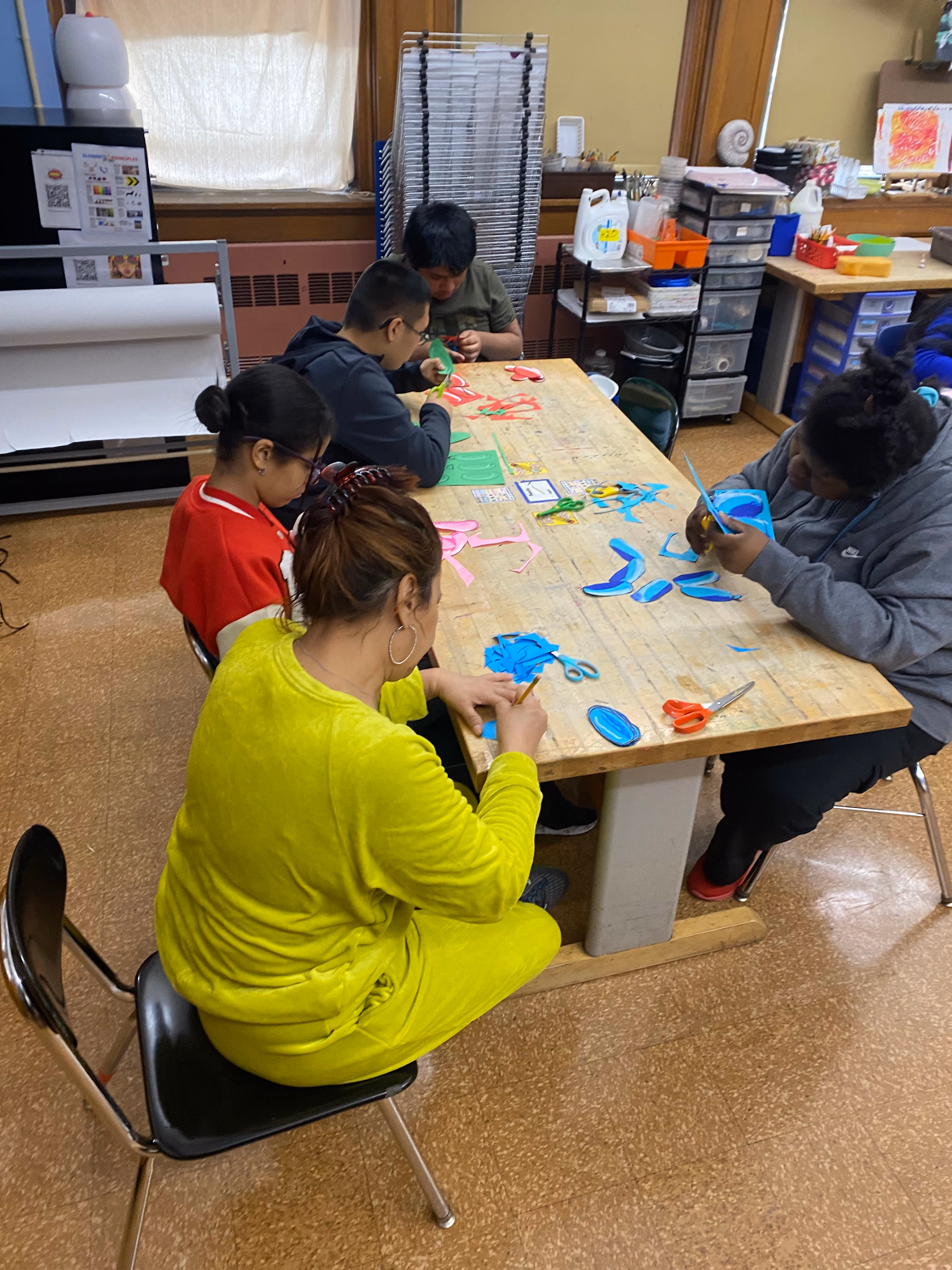 Students and adults cutting colorful shapes during an art class