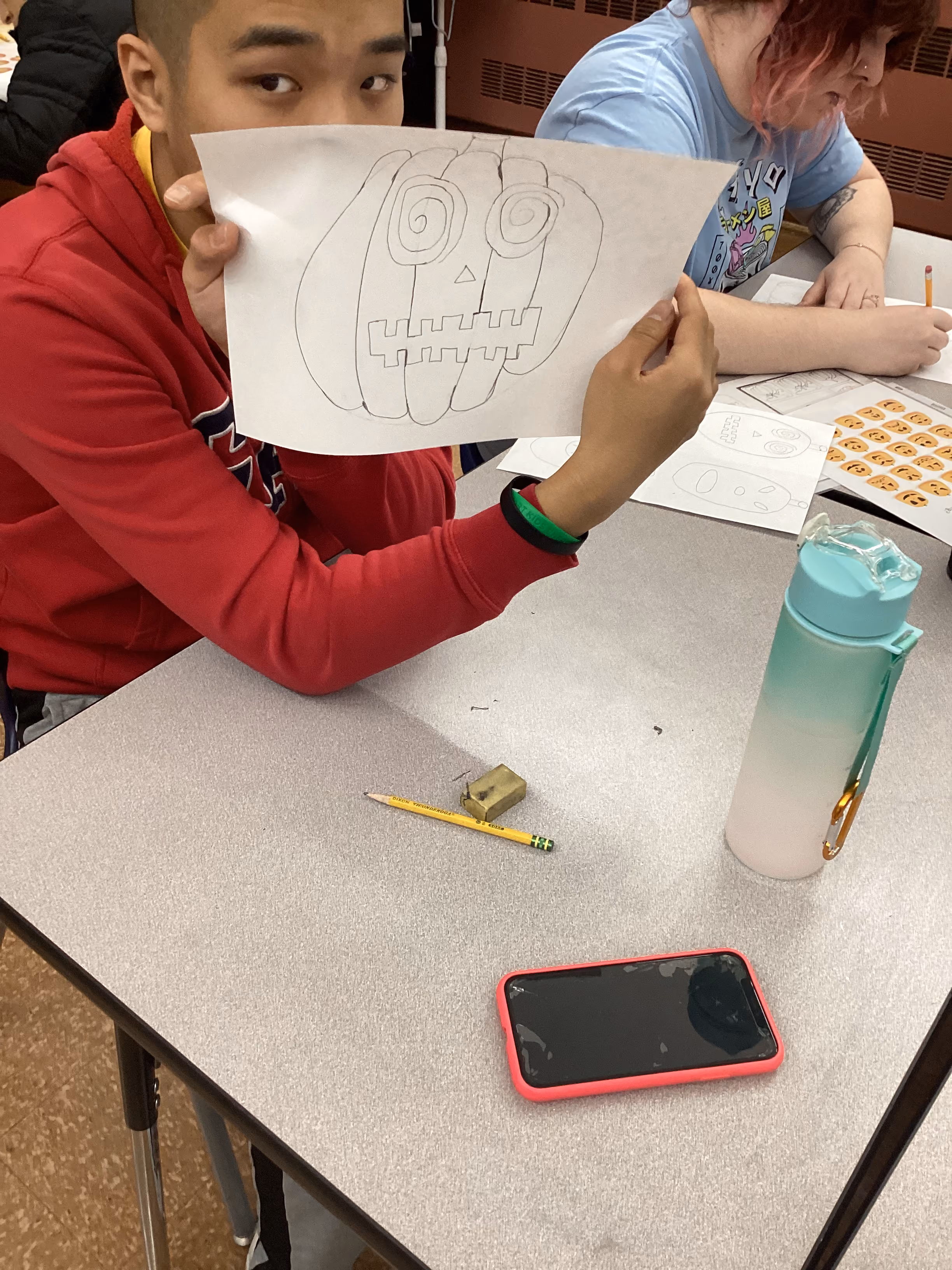 Student holding up a hand-drawn jack-o-lantern pumpkin sketch in class