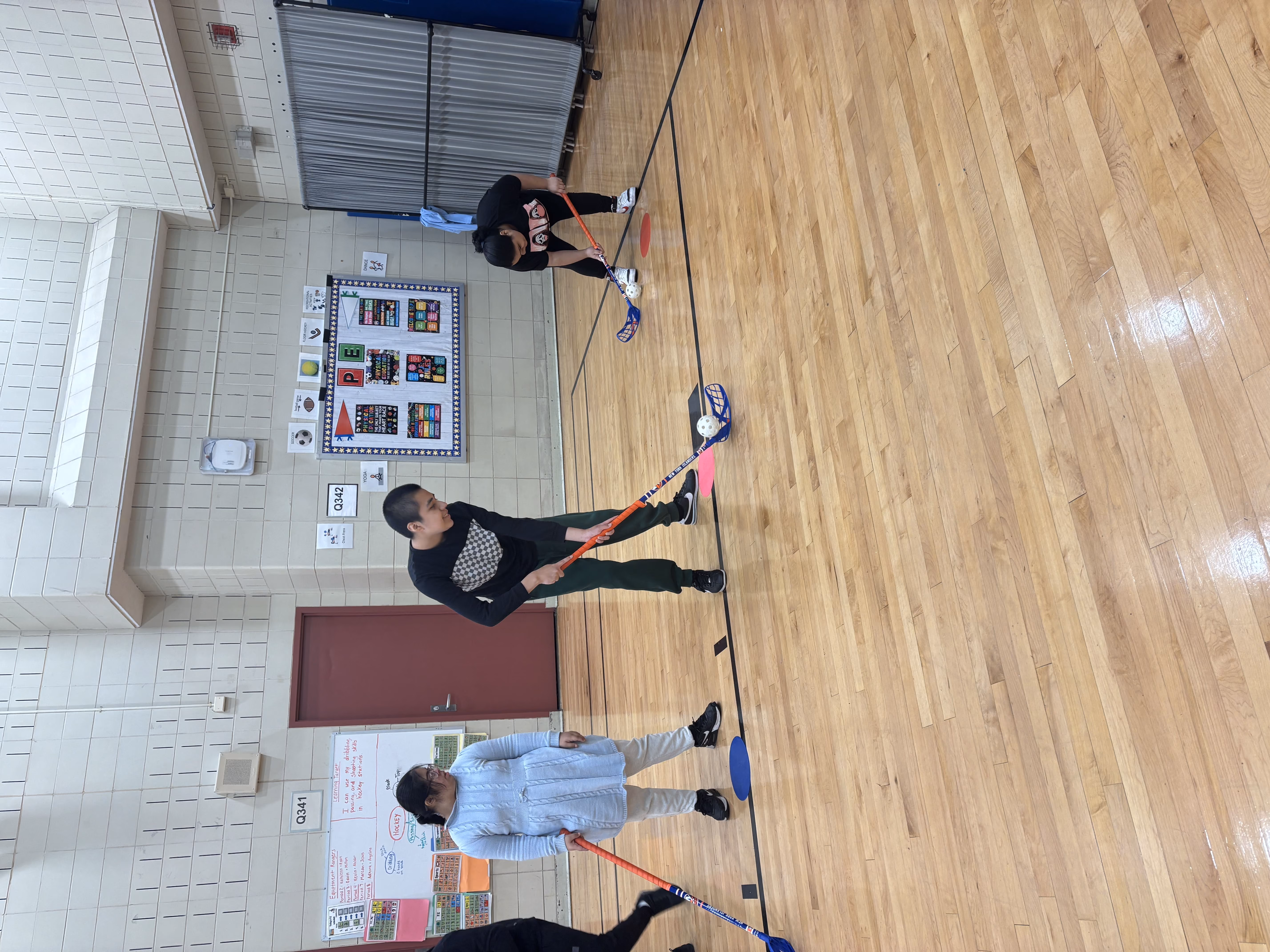 Students playing floor hockey with sticks in school gymnasium
