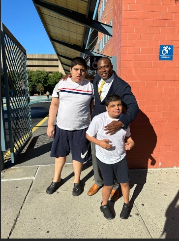 Principal posing with two students outside school building
