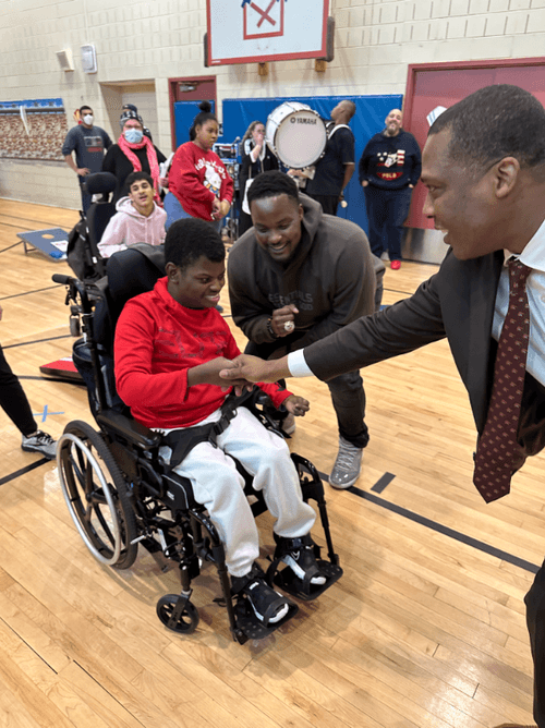 Principal greeting student in wheelchair during school gym event