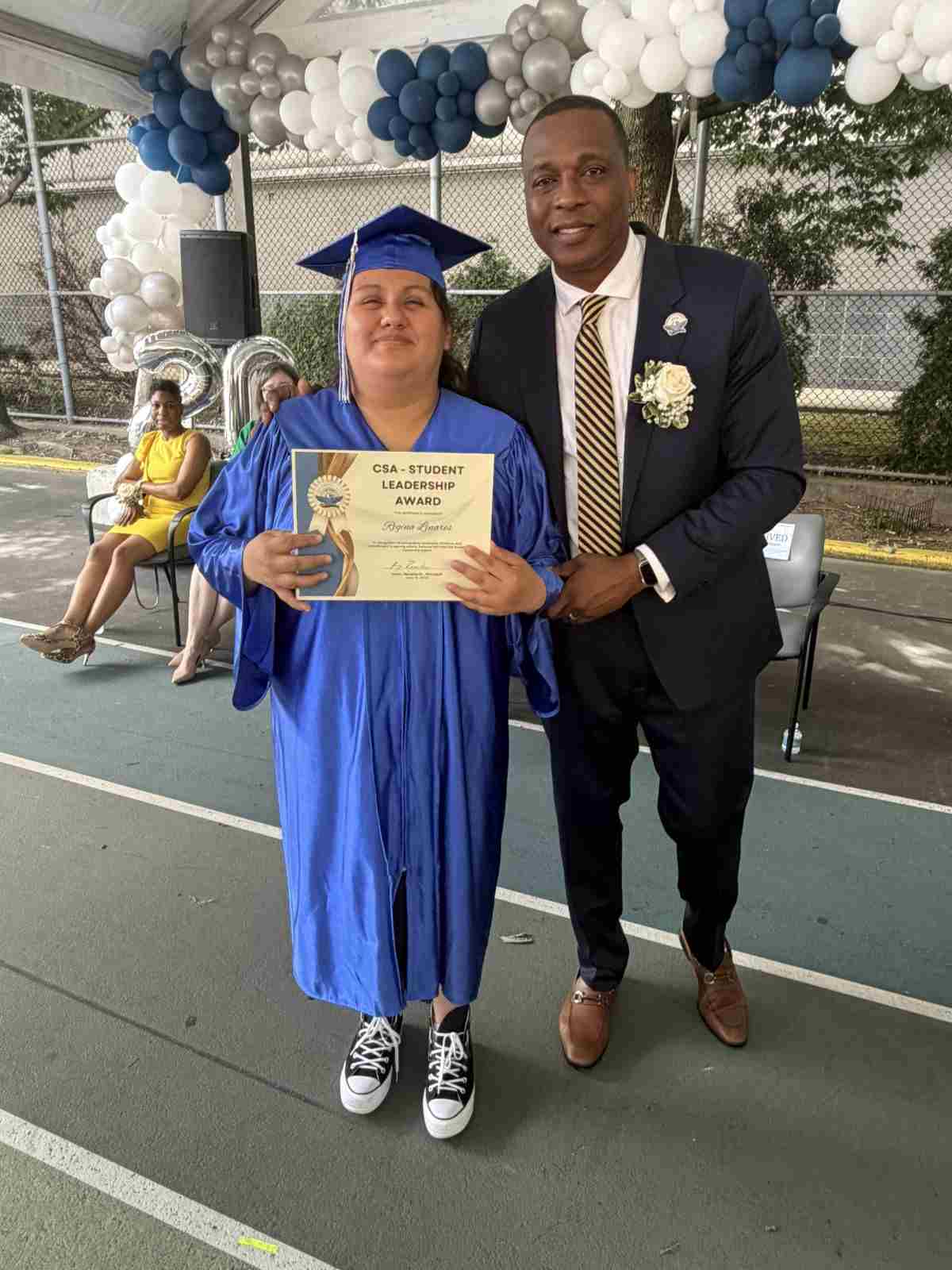 Student in blue cap and gown receives diploma at graduation ceremony