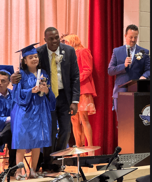 Student in blue cap and gown receives diploma on graduation stage