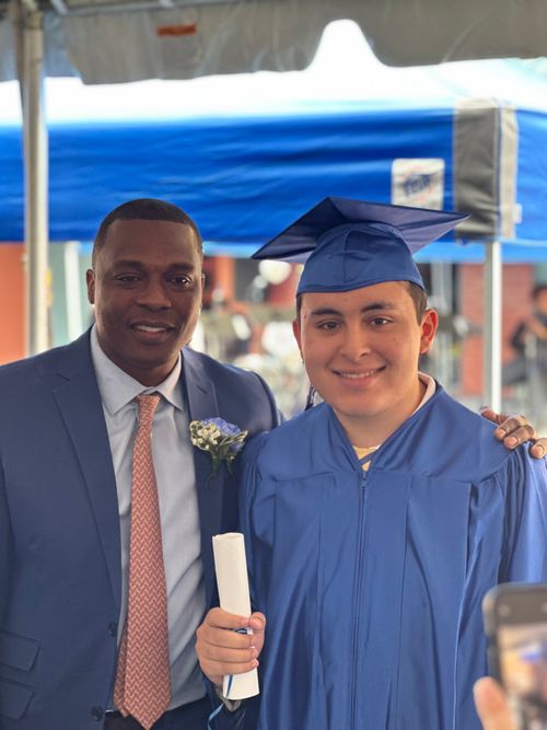 Graduate in blue cap and gown holds diploma with school principal