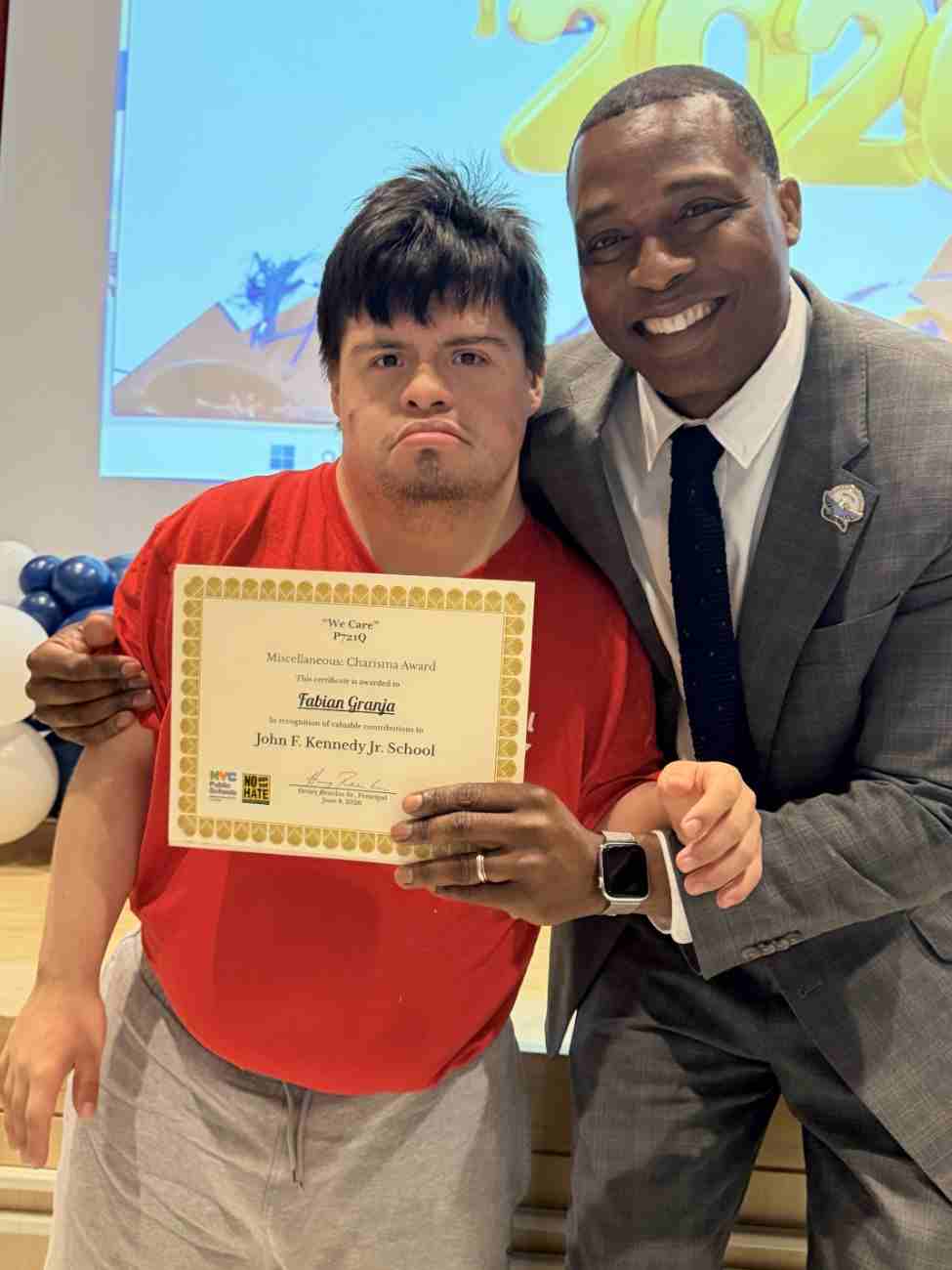 Student holding certificate posing with school principal outdoors