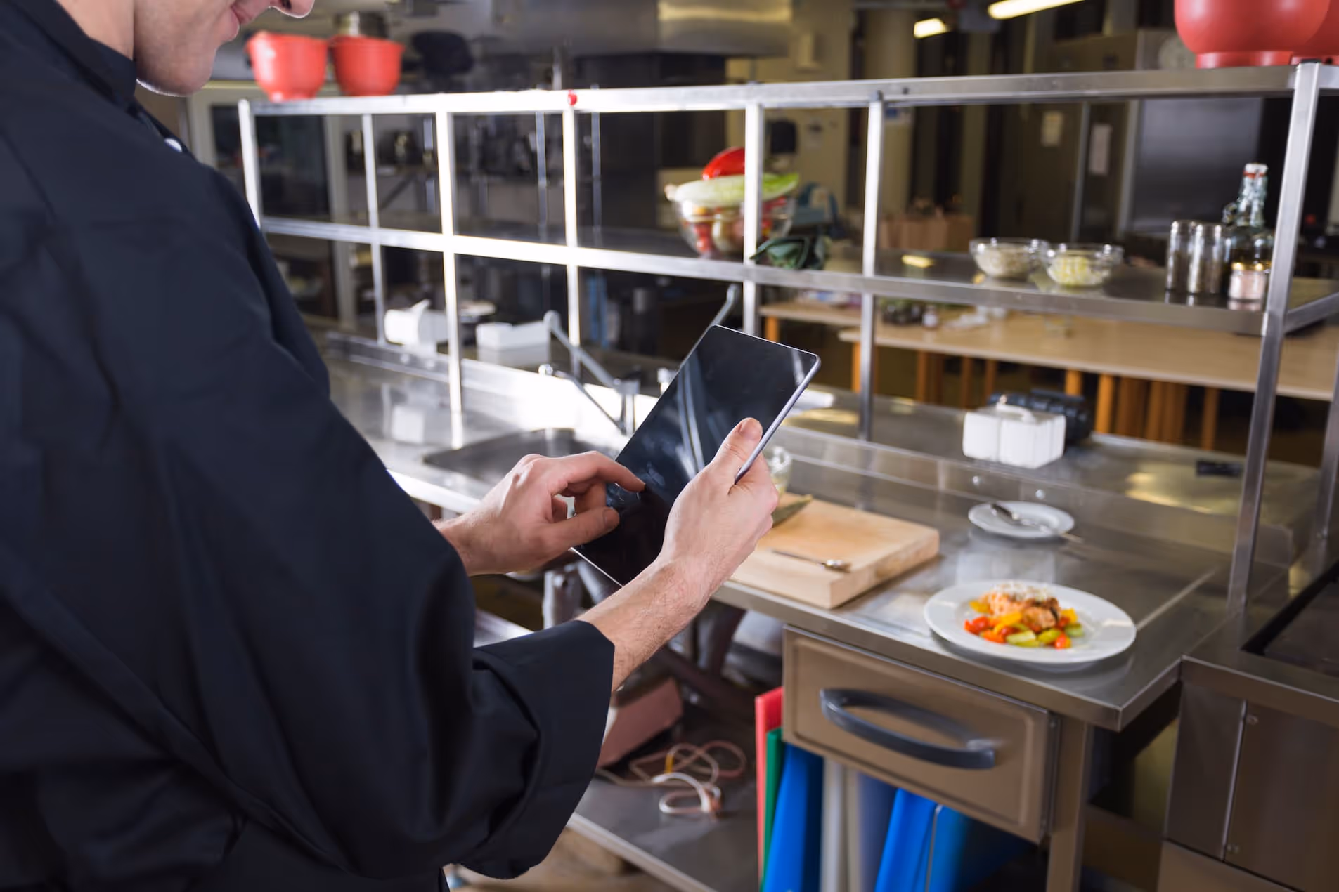 chef with tablet inside commercial kitchen with food on prep table