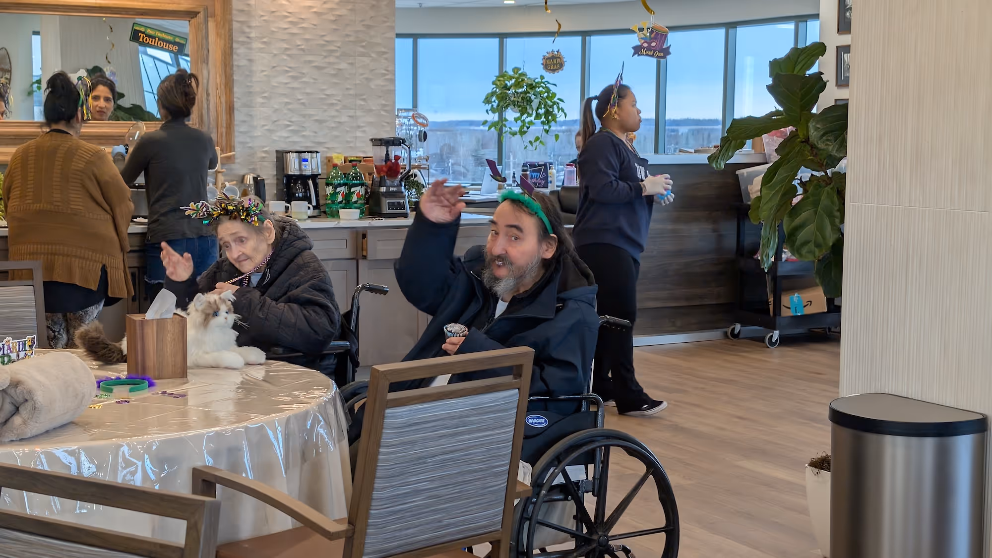 A resident of The Emerald in a wheelchair raises his hand to wave for the camera. He is attending a party.