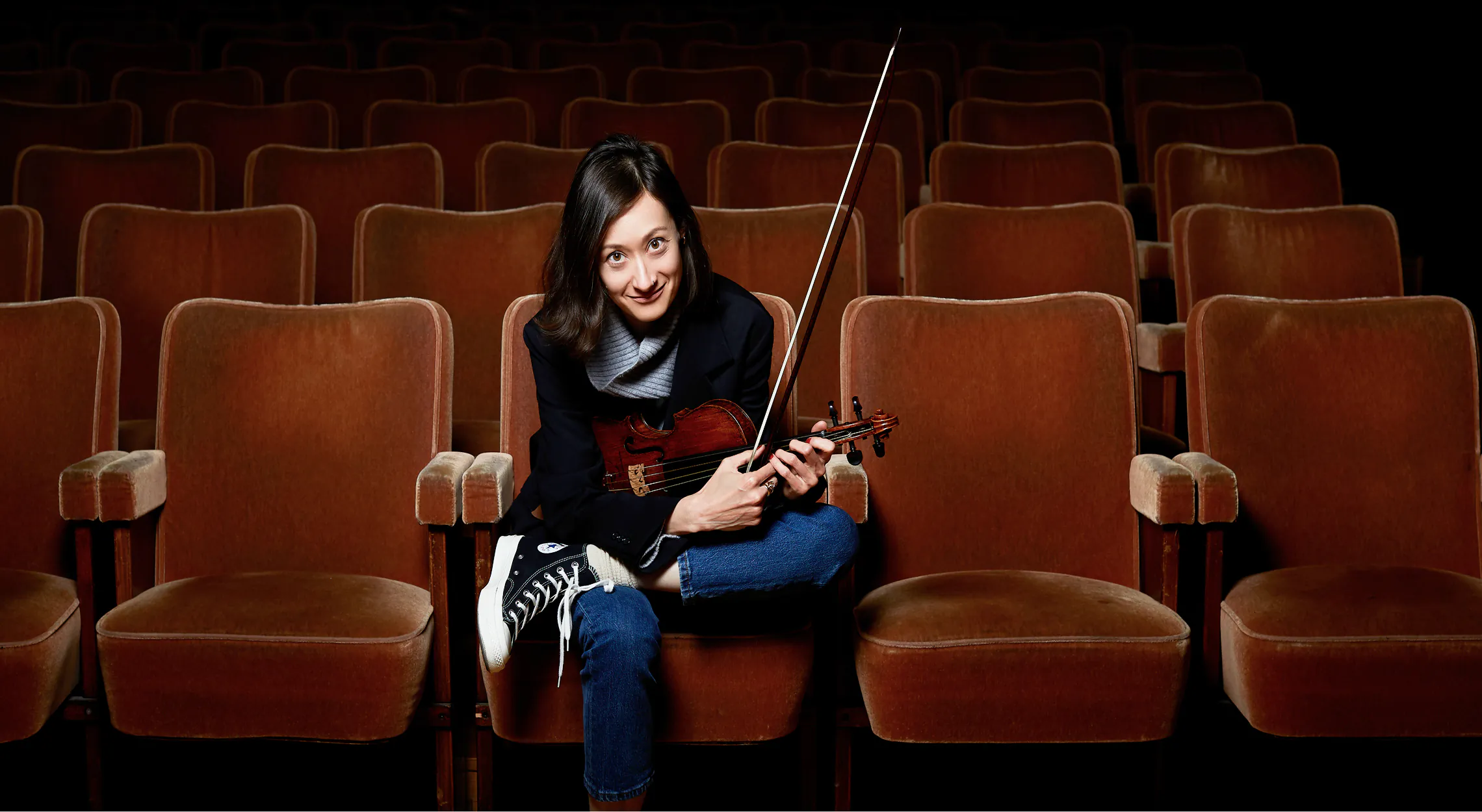 Joanna sitting in a theater holding a violin.