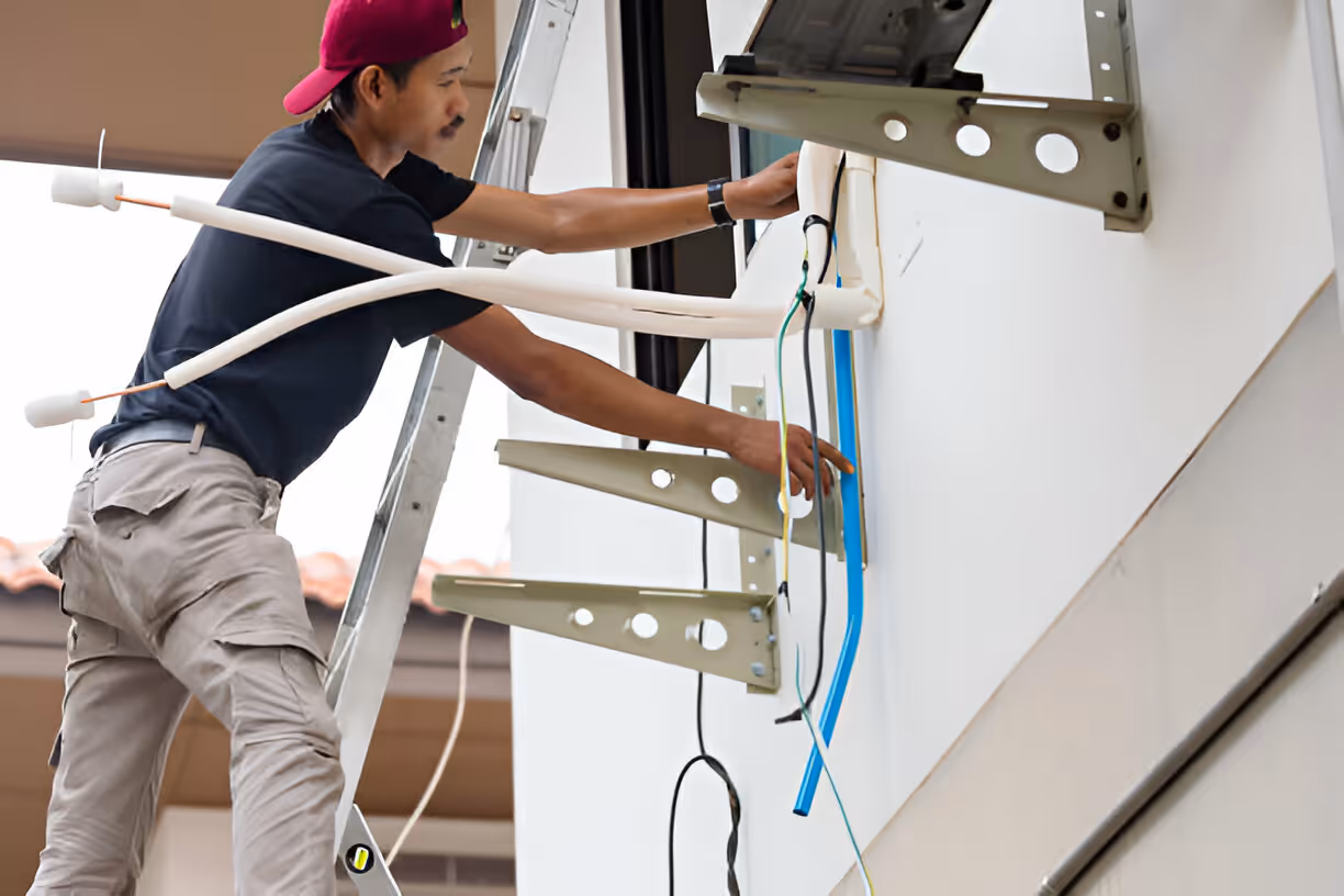 A technician is on a ladder, installing brackets to hold a new mini split system.