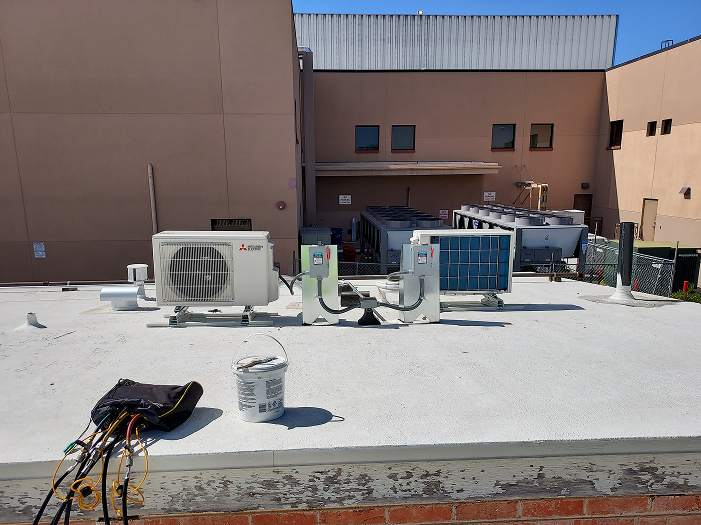 Mitsubishi air conditioning units on a rooftop, with a building and cooling systems in the background.
