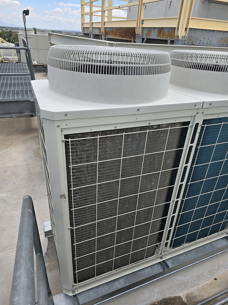 Rooftop air conditioning unit with cooling fins and protective grating, part of a commercial building's HVAC system.
