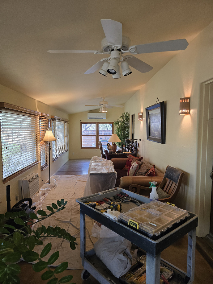 A well-lit living room undergoing renovations with tools on a cart and furniture covered for protection.
