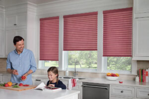 Fun red blinds in three windows above the kitchen sink, with a child sitting at the kitchen island and her dad watching over her