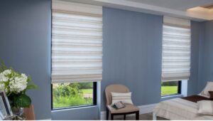 A bedroom with two windows that have white Roman shades