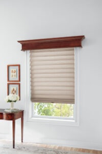 Image of a window with beige Roman shades with a wooden end table next to the window.