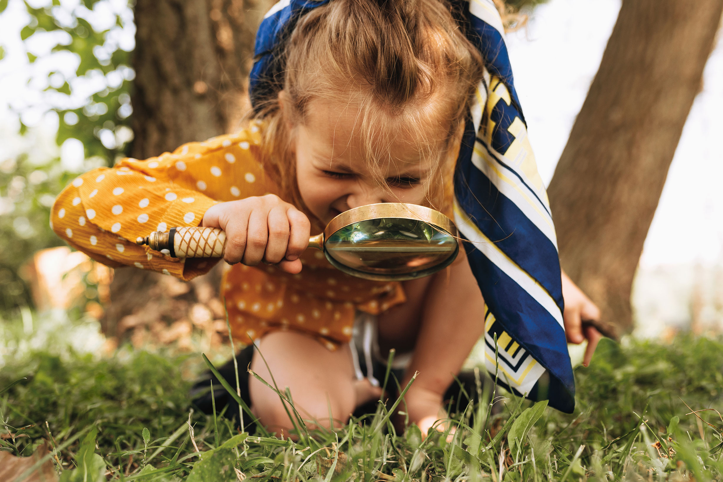 Young girl crouching in the grass using a magnifying glass to explore her surroundings