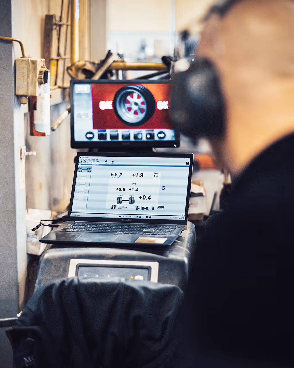 A person is is looking at laptop and a screen displaying tires and numbers.