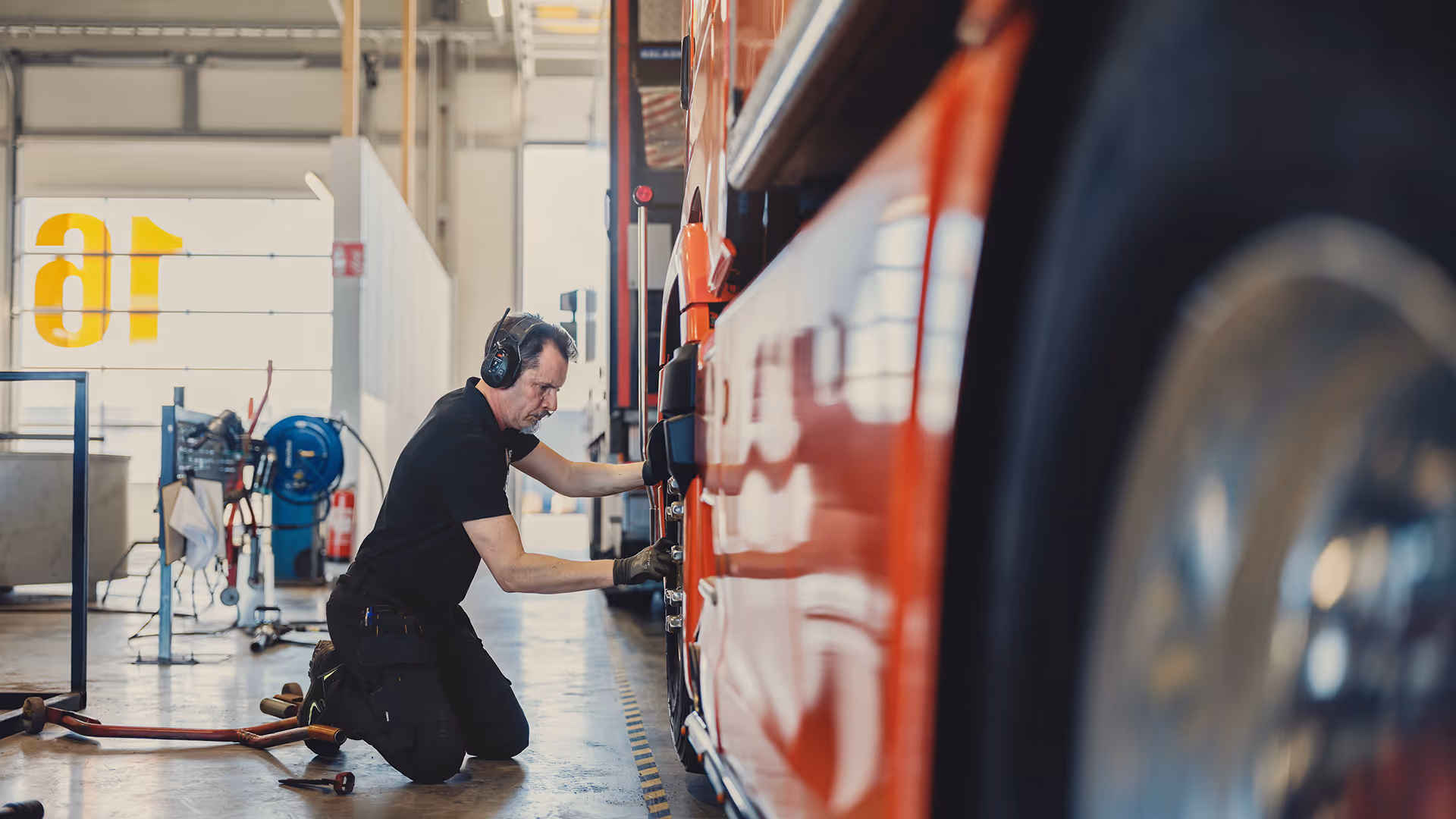 A bright service center where a man is on his knees working on a tire on a red truck.
