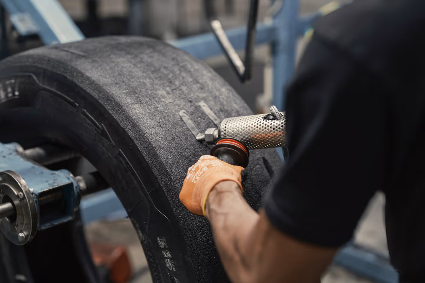 Worker in orange gloves buffing the surface of a large tire using a handheld power tool.