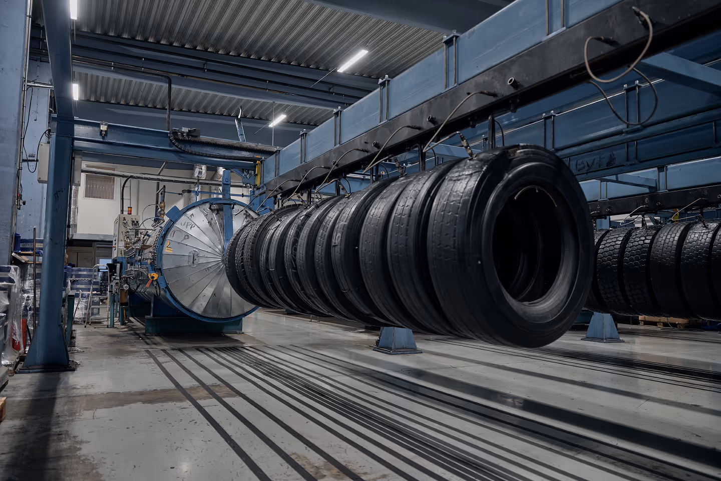 Industrial facility with a row of hanging car tires undergoing manufacturing or testing under a blue metal support structure.