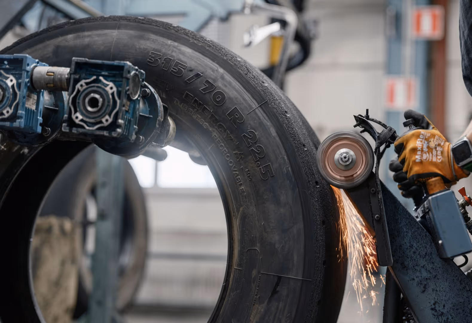 Machine buffing and removing old tread from large tire with sparks flying from the grinding wheel.