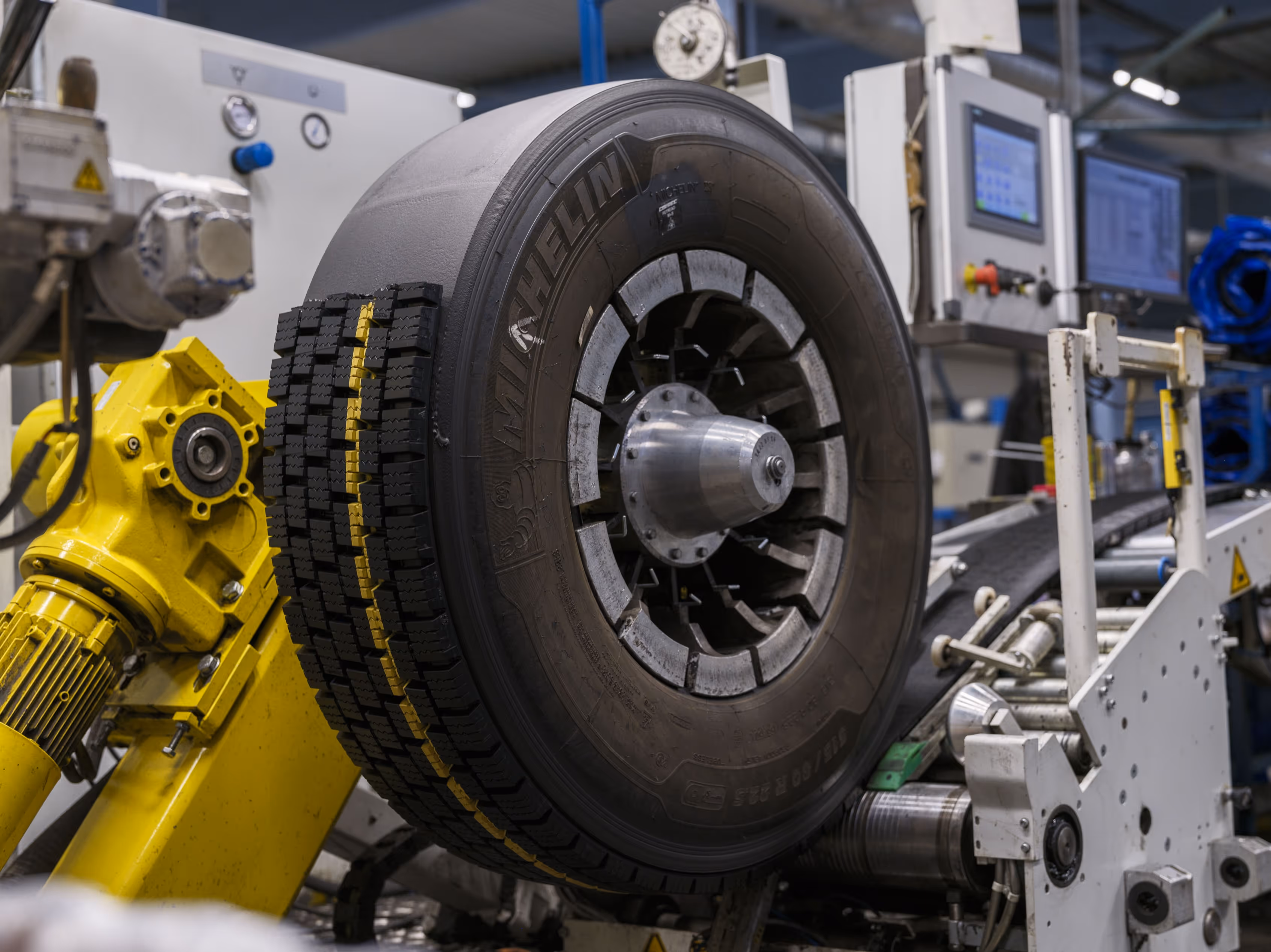 Large tire with new tread pattern on yellow industrial machinery in factory setting.