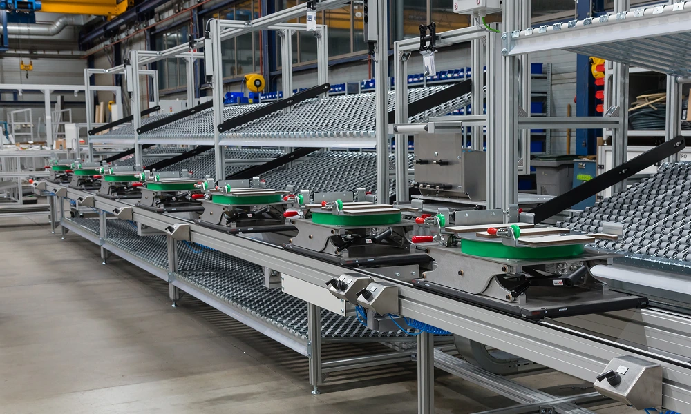 Langlopende productielijn met geavanceerde ophanginstallaties en metalen rollenbanen in een fabriekshal.