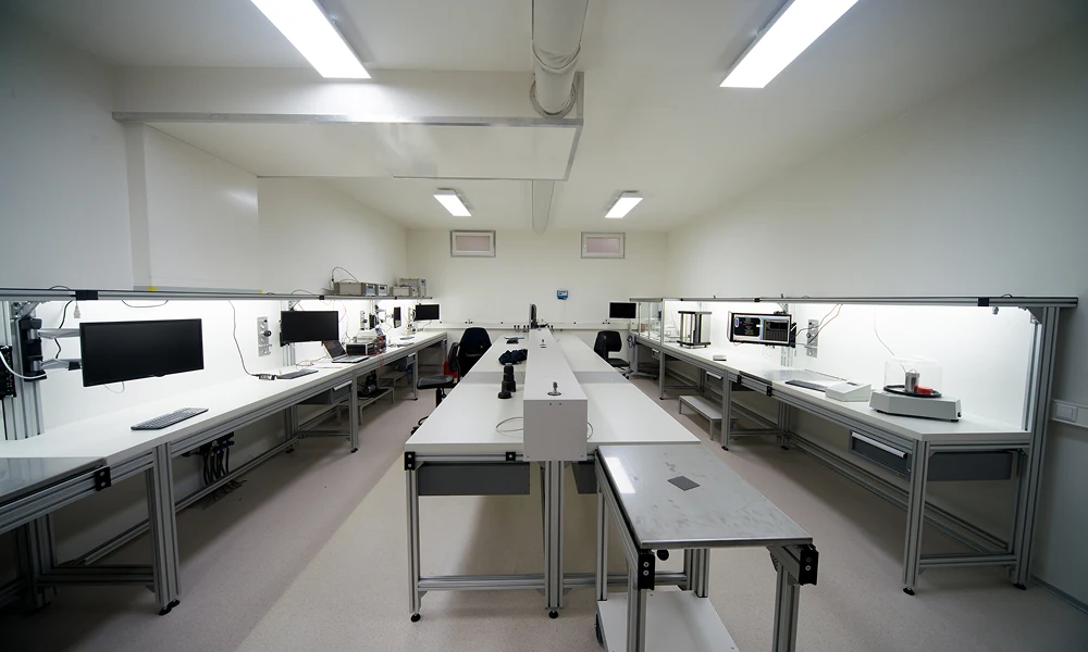 Laboratorium met lange werktafels aan weerszijden, computerschermen en wetenschappelijke apparatuur onder witte TL-verlichting.