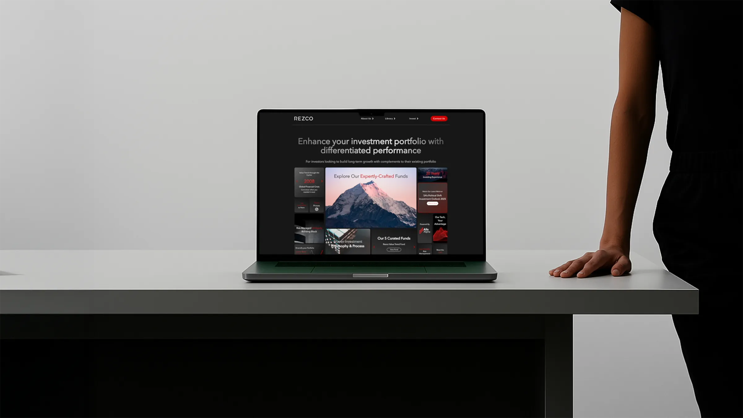 Laptop on a white table displaying an investment portfolio website with a person standing beside the table.
