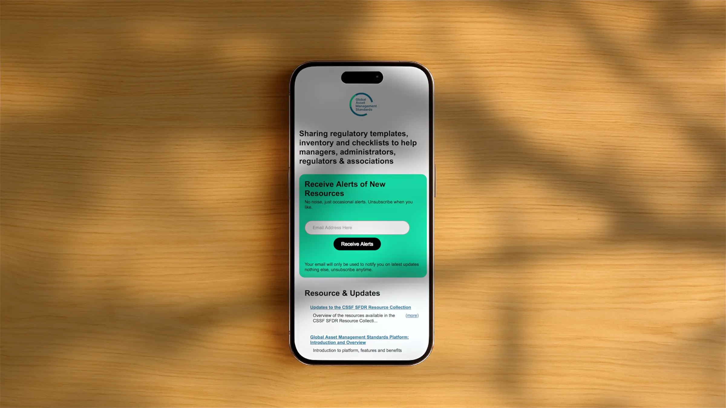 Smartphone on a wooden surface displaying a webpage for sharing regulatory templates, with a green subscription box to receive alerts of new resources.