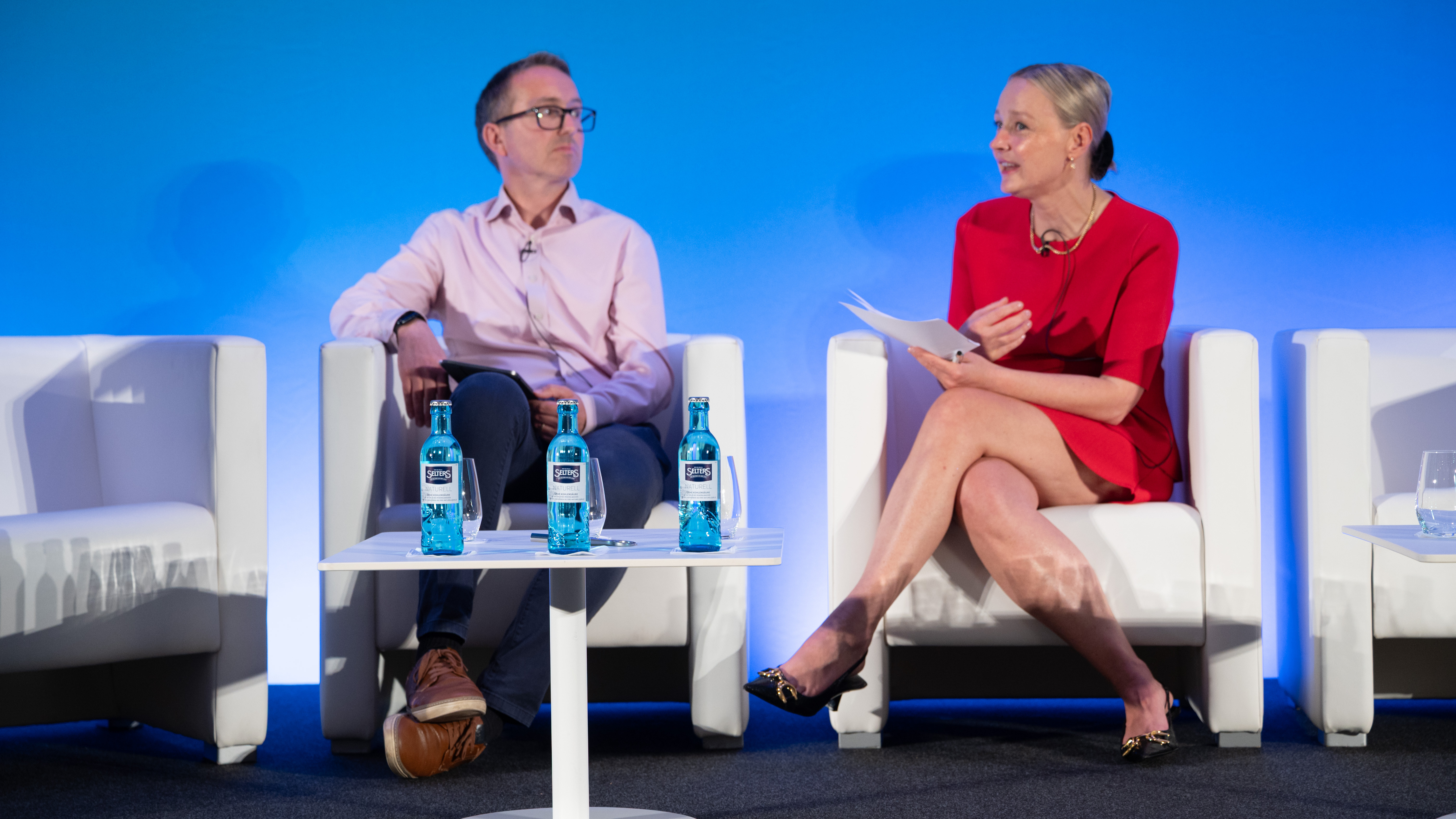 Two people seated on stage for a television-style interview