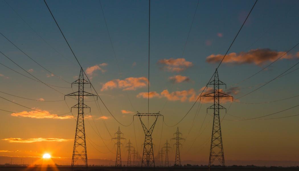 Silhouette of electrical power lines and pylons against a sunset sky