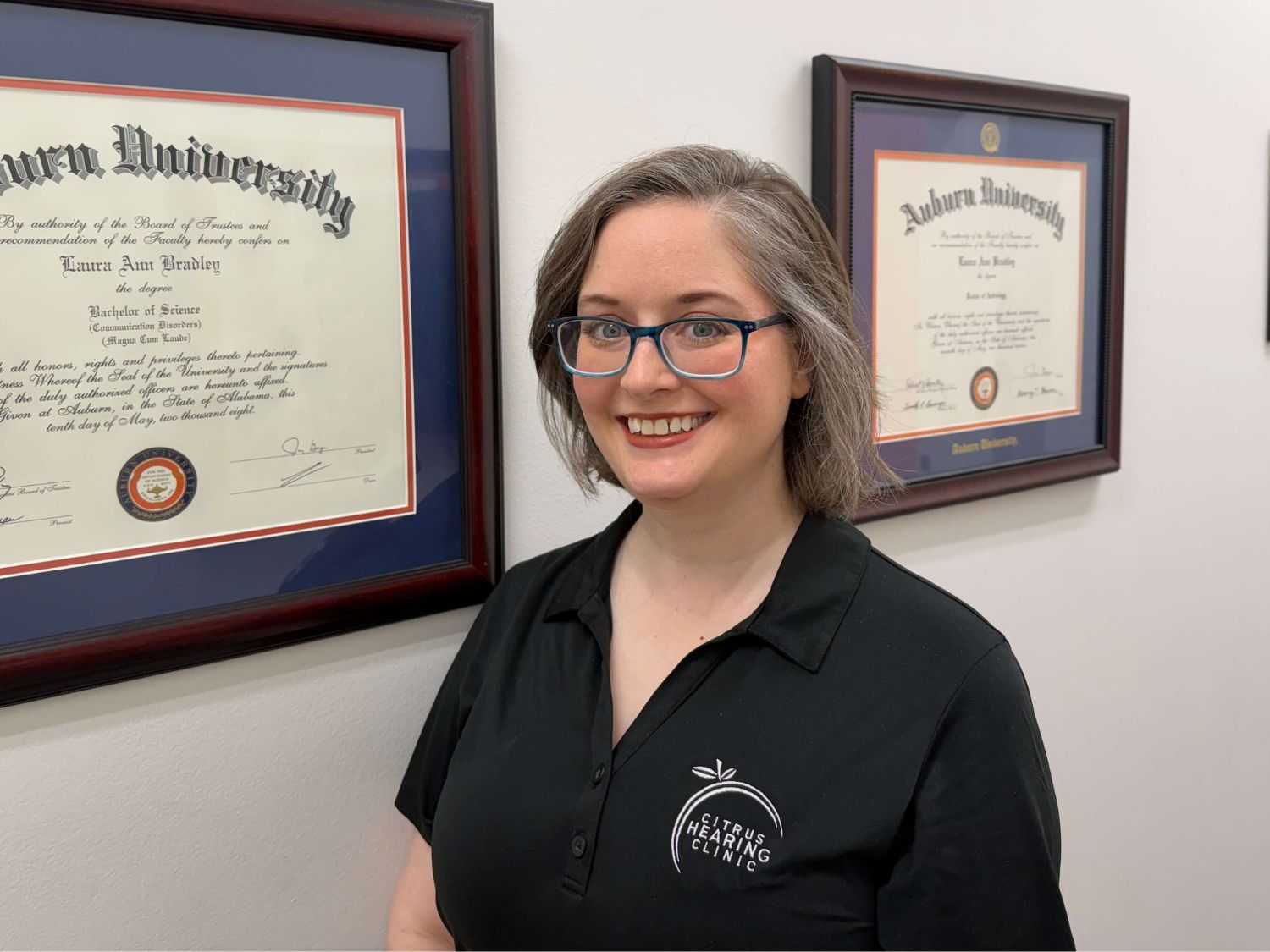 Dr Laura and Dr Teresa wearing black Citrus Hearing Clinic uniforms and glasses standing outdoors.